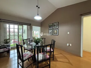 Uma sala de jantar com mesa de vidro e cadeiras de madeira em um imóvel no Brasil.