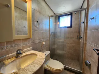 Banheiro com bancada de mármore e box de vidro transparente.