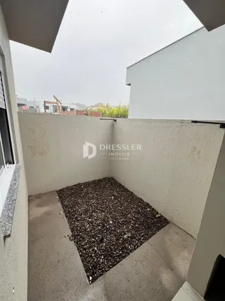 Vista externa de uma área com piso de concreto e cascalho.