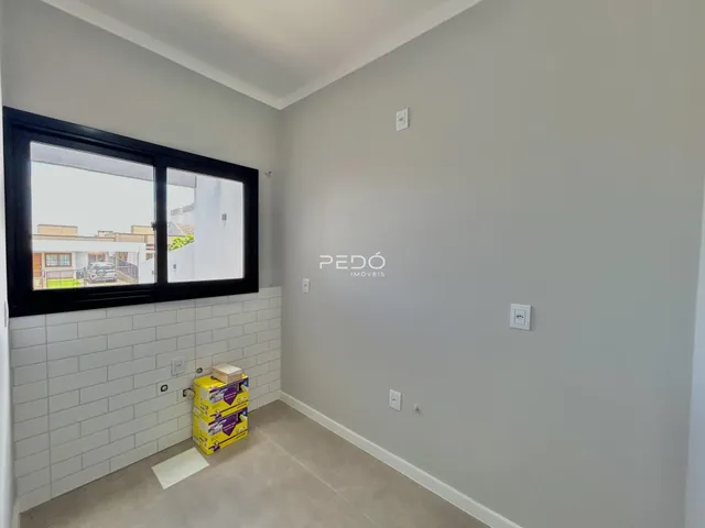 Vista interna de uma sala com parede de tijolos brancos e janela grande.