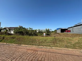 Vista externa de uma propriedade com terreno gramado e estruturas ao fundo.