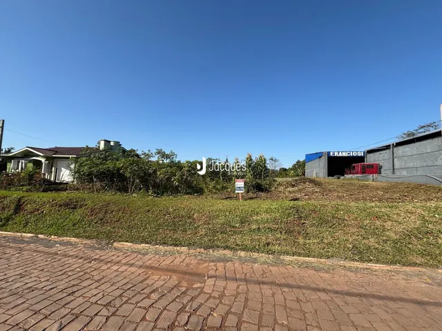 Vista externa de uma propriedade com terreno gramado e estruturas ao fundo.