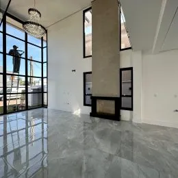 Interior de uma sala ampla com piso de porcelanato e grandes janelas.