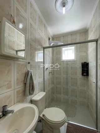 Banheiro com azulejos brancos e box de vidro transparente.