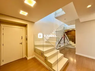 Hall de entrada com piso de madeira e escadaria de vidro em um imóvel em Lajeado.