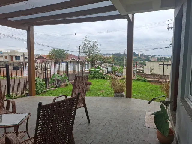 Área externa pavimentada com móveis de vime e vista para o quintal.