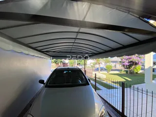 A foto mostra a parte inferior de um telhado e um carro estacionado em frente a uma cerca.