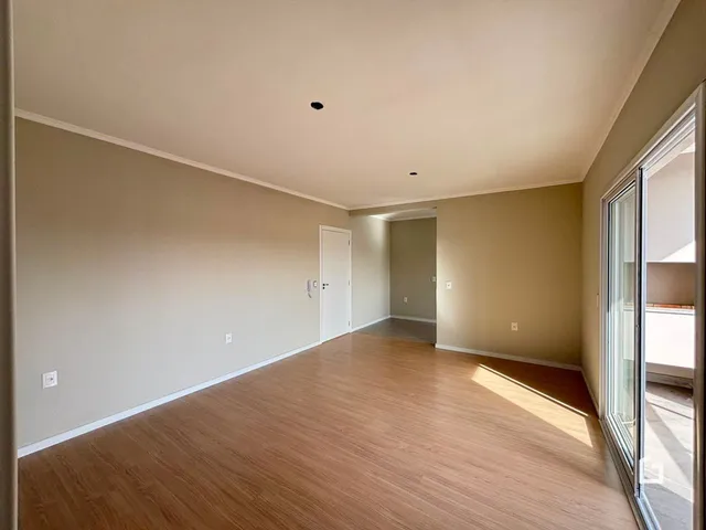 Imagem de uma sala ampla com piso de madeira clara e paredes neutras.