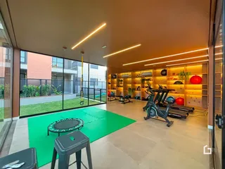 Interior de uma área comum com equipamentos de ginástica e grandes janelas de vidro.
