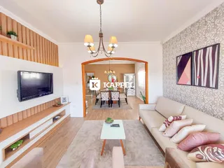 Sala de estar com sofá claro e televisão montada na parede de madeira.