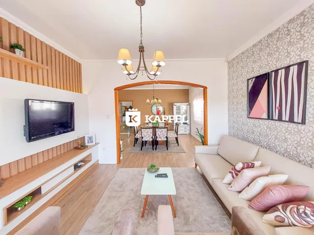 Sala de estar com sofá claro e televisão montada na parede de madeira.