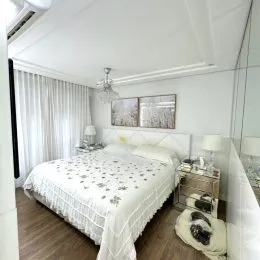 Quarto com cama de casal e cortinas brancas.