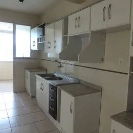 Foto de uma cozinha com armários superiores e bancadas brancas.