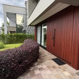Fachada de uma residência com revestimento vertical marrom e paisagismo.