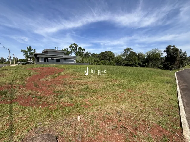 Vista externa de uma propriedade com terreno gramado e casa ao fundo.