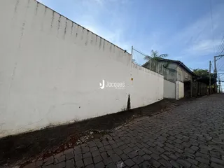 Parede branca de um imóvel com cerca de metal e calçada de paralelepípedos.