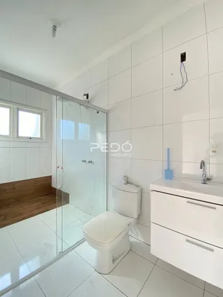 Foto de um banheiro com piso e paredes brancas e box de vidro.