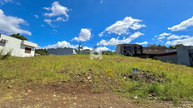 Vista externa de uma propriedade com terreno gramado e construções ao fundo.