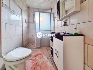 Interior de um banheiro com revestimento de azulejos brancos e um vaso sanitário.