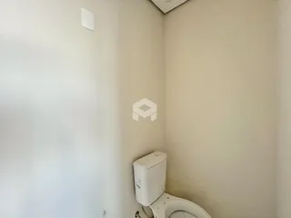 A foto mostra uma parede branca com um vaso sanitário em um ambiente interno.