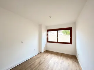 Uma foto de um cômodo interno com paredes brancas e piso de madeira clara.