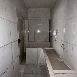 Corredor interno com revestimento de azulejos brancos nas paredes e piso.