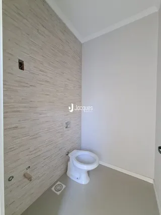 Uma parede de banheiro com azulejos claros e um vaso sanitário branco são visíveis.