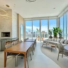Ambiente interno com mesa de madeira e grandes janelas em um apartamento.
