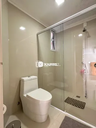 Interior de um banheiro com vaso sanitário e box de vidro transparente.