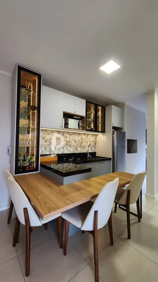 A sala de jantar apresenta uma mesa de madeira com cadeiras brancas.