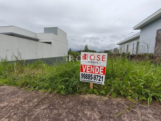 Vista externa de uma propriedade com vegetação alta e sinal de venda.
