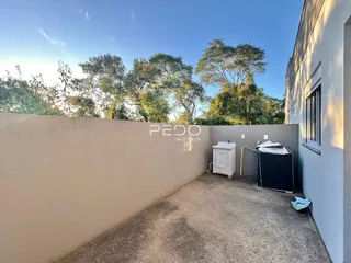 Vista externa de um pátio com muro e vegetação ao lado de uma edificação.