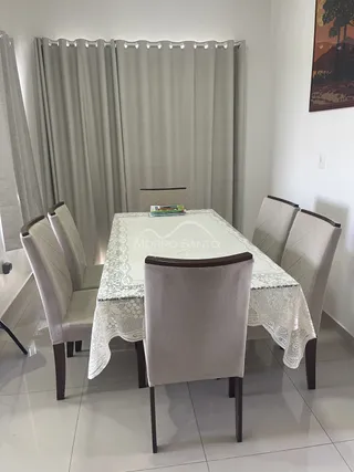 Uma mesa de jantar com cadeiras estofadas e toalha de renda está visível no ambiente.