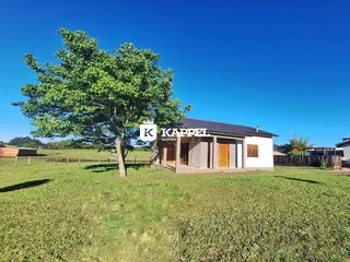 Fachada de uma casa simples em um campo aberto sob um céu azul.