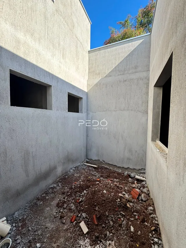 Vista de um canto de construção com paredes de concreto expostas e solo irregular.