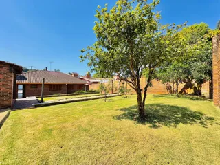 Vista externa de um quintal gramado com uma grande árvore e muros de tijolo.