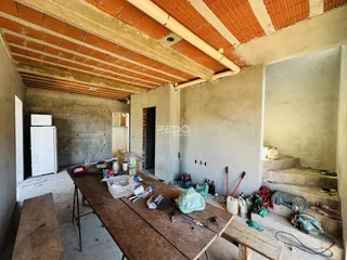 Imagem de um cômodo interno em construção com teto de telhas exposto.