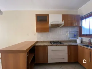 Vista interna de uma cozinha com armários de madeira e revestimento de azulejos