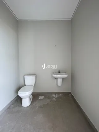 Foto interna de um banheiro com piso de concreto e louças sanitárias brancas.