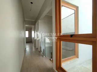 Corredor interno de uma residência com piso de madeira clara.