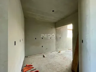 Interior de um ambiente em construção com paredes brancas e piso de concreto aparente.