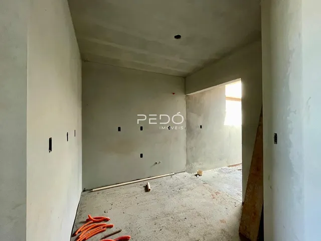 Interior de um ambiente em construção com paredes brancas e piso de concreto aparente.