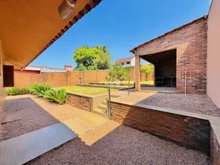 Vista externa de um jardim com muro de tijolos e área de convivência.