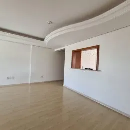 Ambiente interno de uma sala ampla com piso de madeira clara e paredes brancas.