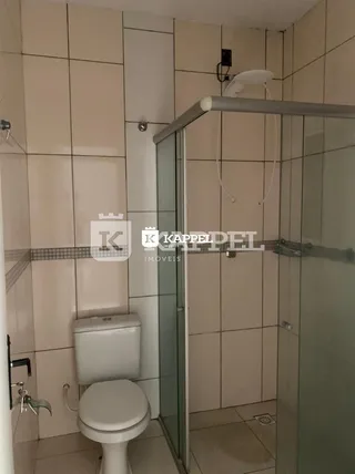 Foto interna de um banheiro com revestimento de azulejos brancos e box de vidro.