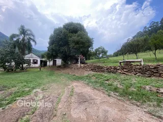 Vista externa de uma propriedade rural com muro de pedra e vegetação.