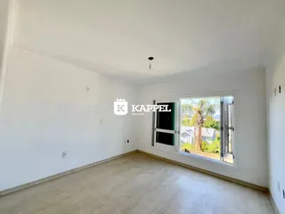 Uma sala ampla com piso de madeira clara e uma grande janela voltada para o exterior.