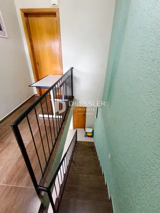 Hall de entrada com porta de madeira e corrimão preto.