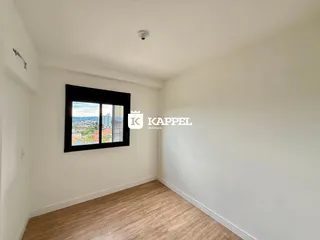 Uma foto interna mostra um cômodo com piso de madeira e uma grande janela com vista para a cidade.