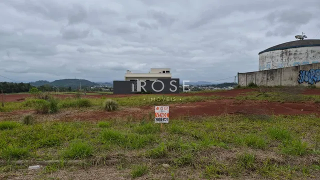 Vista externa de uma propriedade com terreno gramado e estruturas ao fundo.